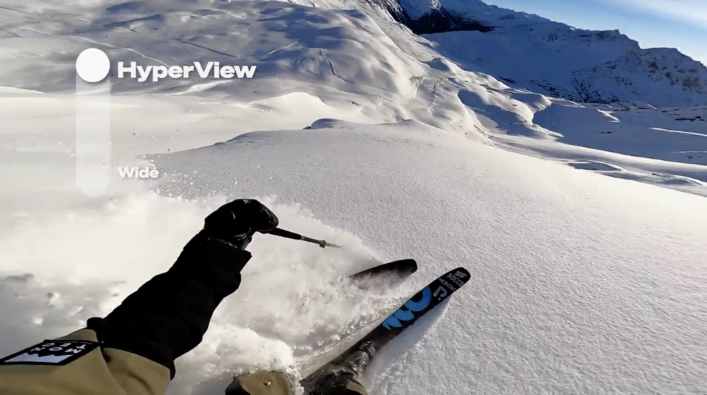 Skier riding fresh powder using a GoPro Hero11 Black mounted to their head. The on screen graphic shows the HyperView Digital Lens selected in this tutorial video 